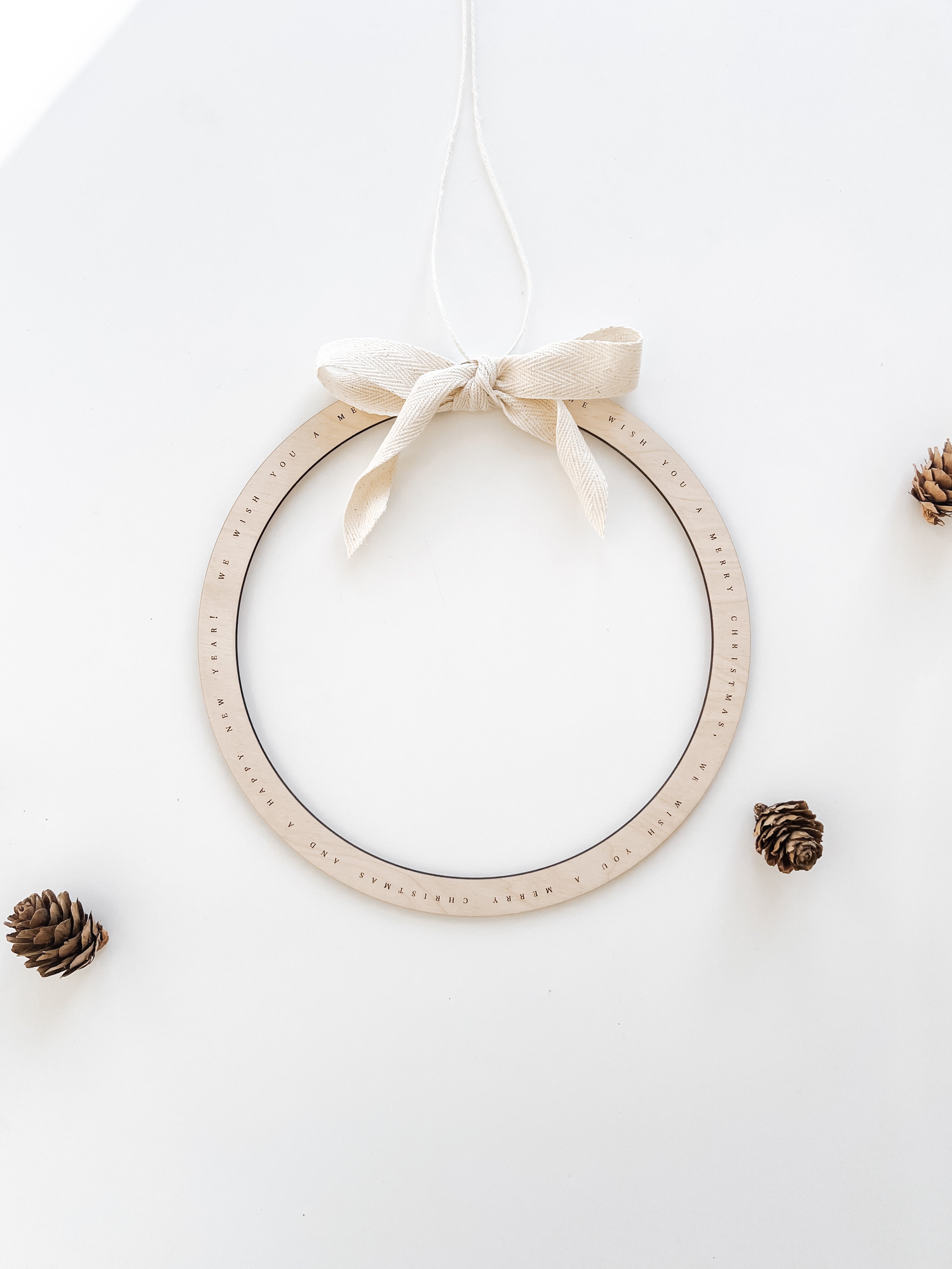 Weihnachtlicher Türkranz aus Holz mit „We Wish You a Merry Christmas“-Gravur und naturfarbener Baumwollschleife.
